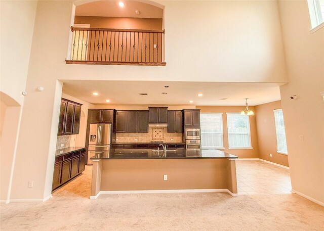 kitchen featuring stainless steel appliances, light carpet, a towering ceiling, and decorative backsplash