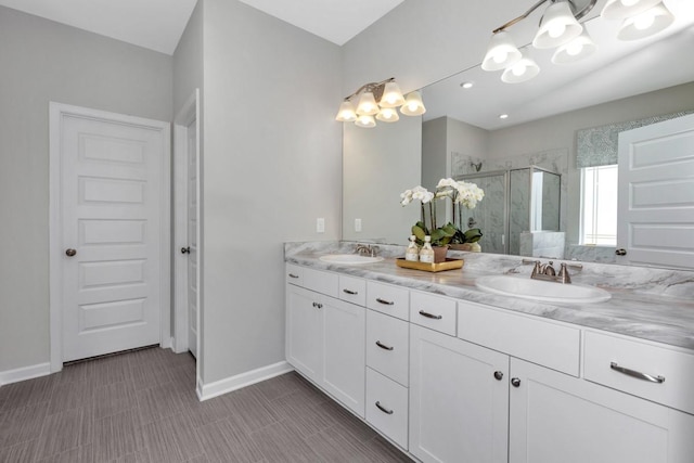 bathroom with a shower stall, double vanity, baseboards, and a sink