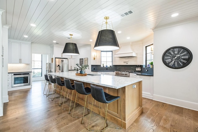 kitchen with custom exhaust hood, light wood-style flooring, backsplash, and appliances with stainless steel finishes