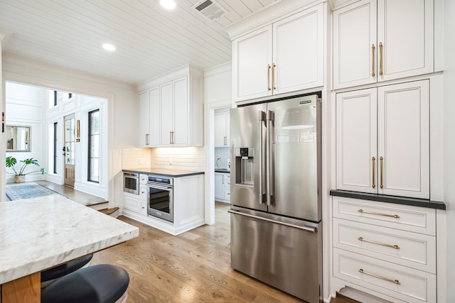 kitchen featuring light wood-type flooring, visible vents, tasteful backsplash, white cabinetry, and appliances with stainless steel finishes