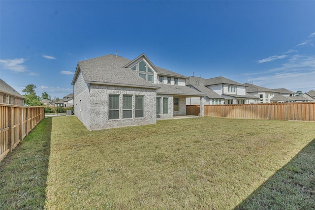 rear view of house featuring a shingled roof, a fenced backyard, brick siding, and a lawn