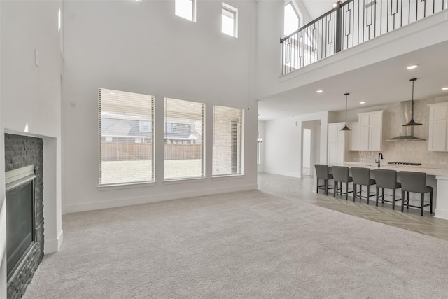 living area featuring baseboards, light colored carpet, a high ceiling, and a glass covered fireplace