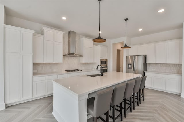 kitchen featuring a sink, a breakfast bar area, stainless steel appliances, wall chimney exhaust hood, and a kitchen island with sink