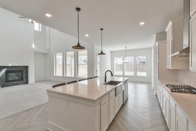 kitchen with stainless steel gas cooktop, a sink, light countertops, a glass covered fireplace, and wall chimney range hood