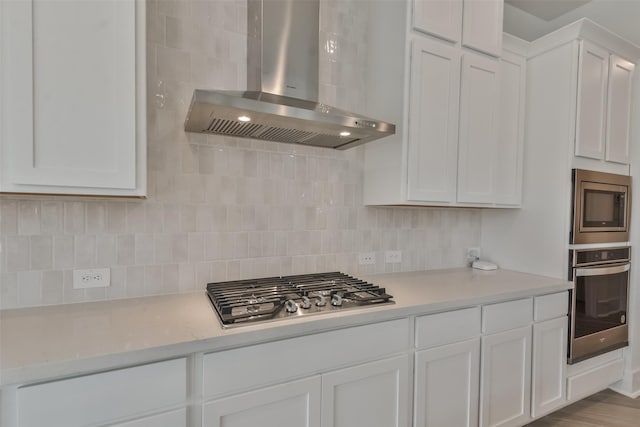 kitchen featuring white cabinetry, light countertops, wall chimney range hood, and appliances with stainless steel finishes