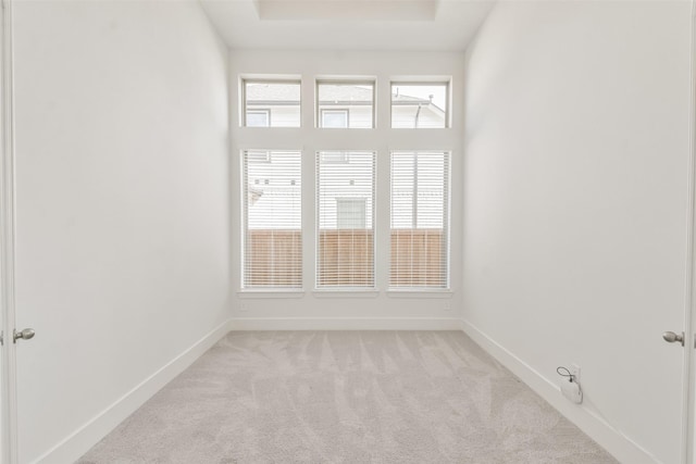 unfurnished room with a raised ceiling, light colored carpet, and baseboards