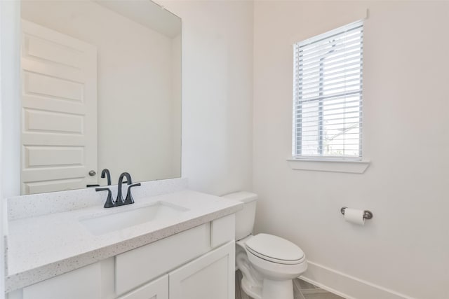 half bathroom featuring toilet, vanity, and baseboards