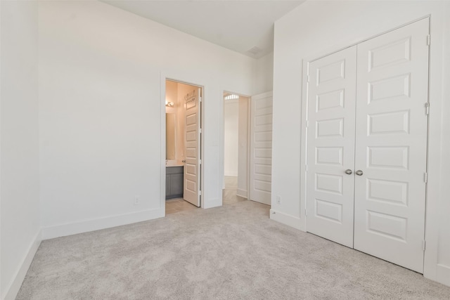 unfurnished bedroom with a closet, carpet floors, baseboards, and ensuite bath