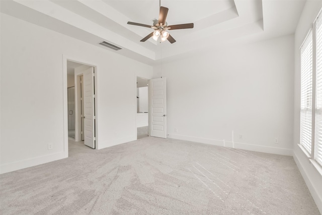 unfurnished bedroom featuring light carpet, visible vents, a raised ceiling, and baseboards