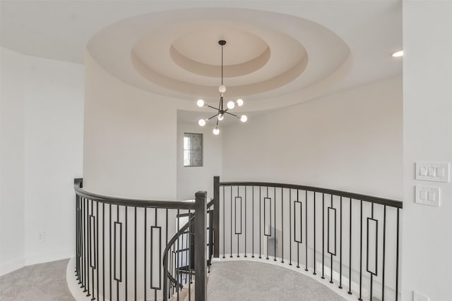 hallway featuring carpet, an inviting chandelier, an upstairs landing, and a tray ceiling