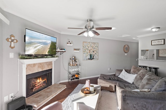 living room featuring a ceiling fan, wood finished floors, a fireplace, crown molding, and baseboards