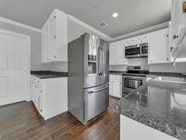 kitchen featuring white cabinets, stainless steel appliances, wood finish floors, and ornamental molding