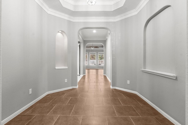 hallway featuring arched walkways, dark tile patterned flooring, baseboards, and ornamental molding