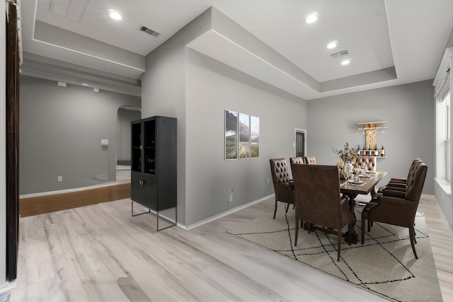 dining space with light wood-type flooring, visible vents, a raised ceiling, and baseboards