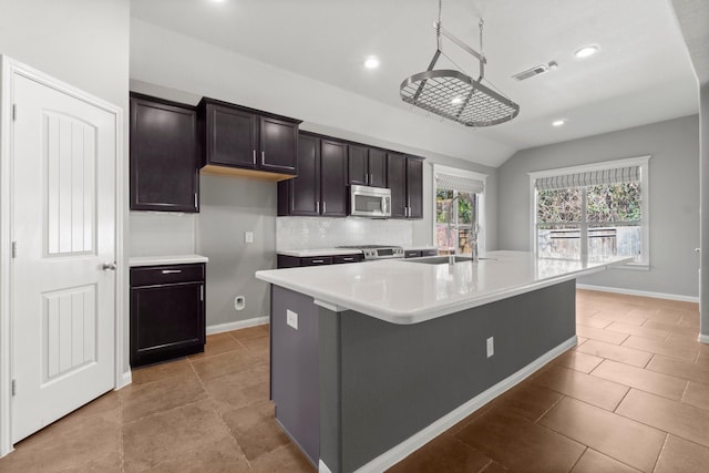 kitchen with visible vents, backsplash, a center island with sink, light countertops, and appliances with stainless steel finishes