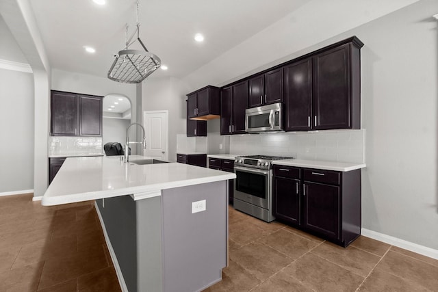 kitchen with tasteful backsplash, an island with sink, arched walkways, stainless steel appliances, and a sink