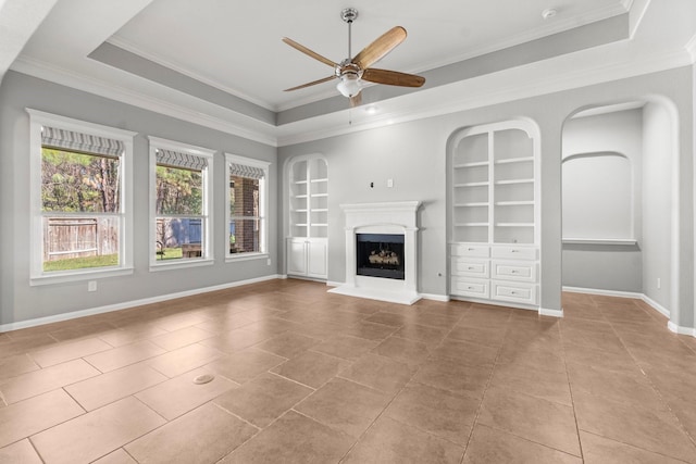 unfurnished living room with built in features, a tray ceiling, and a fireplace with raised hearth