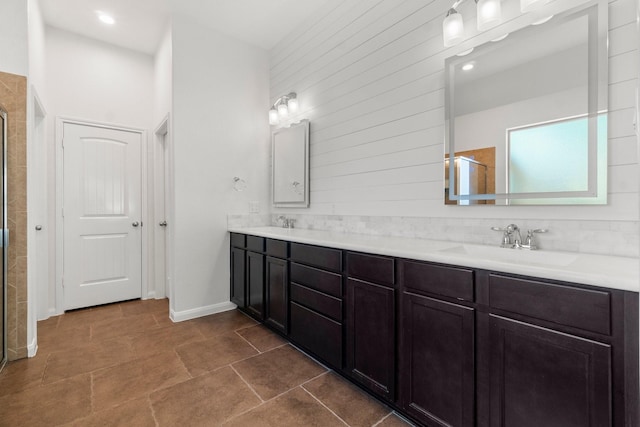 bathroom featuring a sink, baseboards, a shower with door, and double vanity