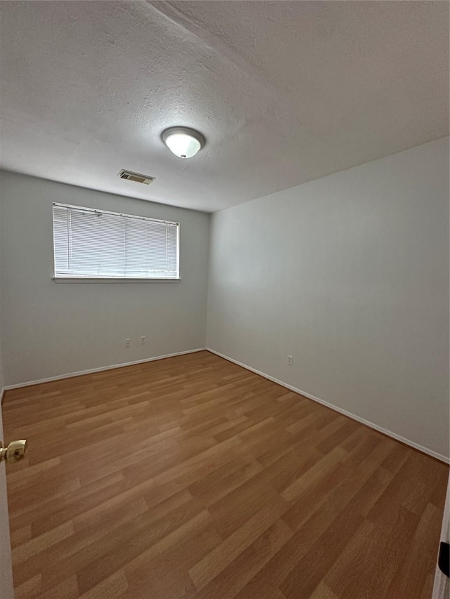 spare room with light wood-style flooring, baseboards, visible vents, and a textured ceiling