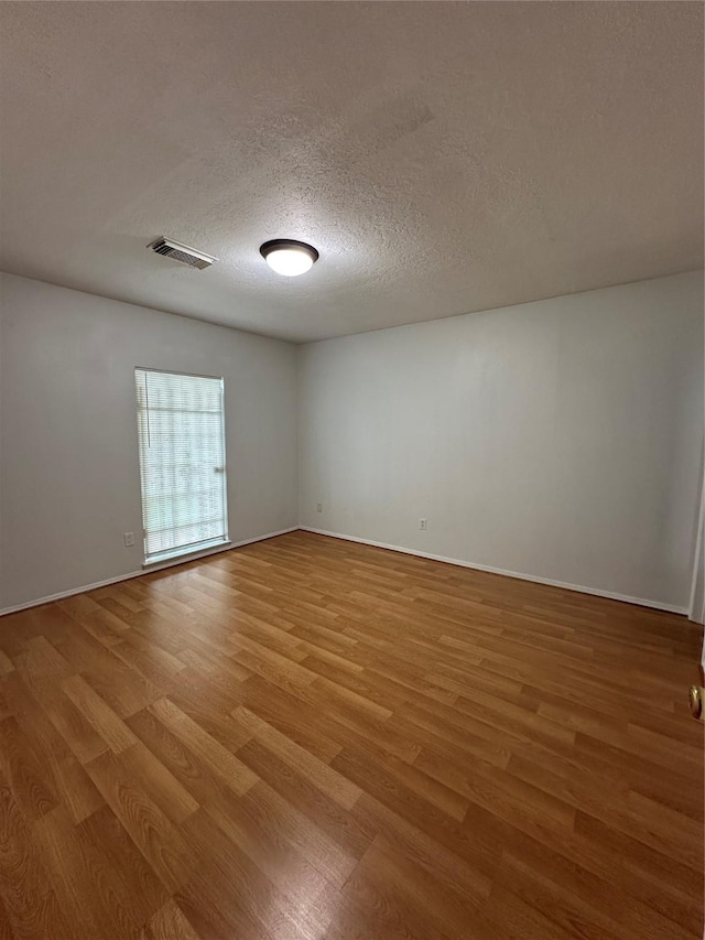 spare room with baseboards, visible vents, a textured ceiling, and light wood-style floors