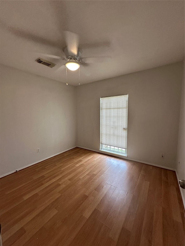 unfurnished room with ceiling fan, visible vents, baseboards, and wood finished floors