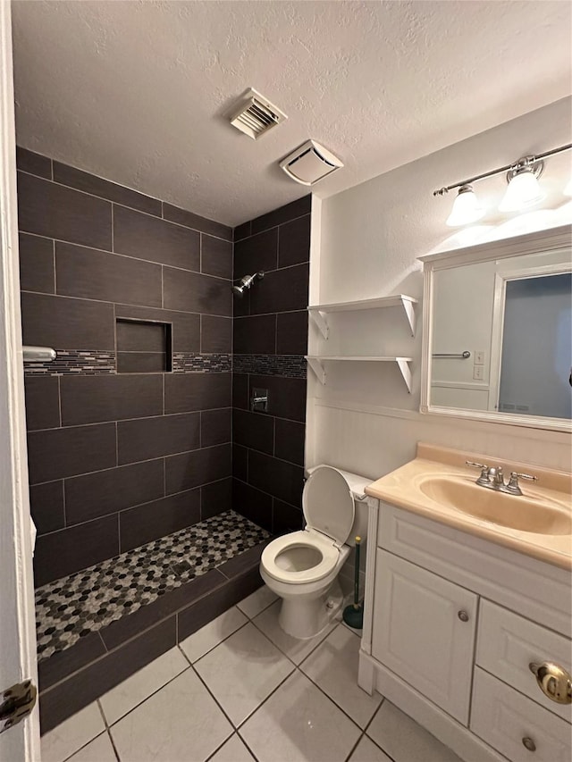 full bathroom featuring vanity, visible vents, a tile shower, a textured ceiling, and toilet