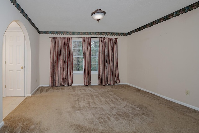 carpeted empty room featuring tile patterned floors, arched walkways, baseboards, and a textured ceiling