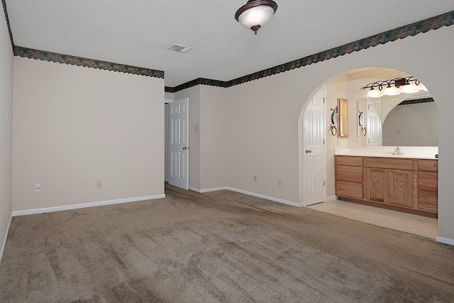 unfurnished bedroom with baseboards, light colored carpet, arched walkways, a textured ceiling, and a sink