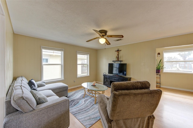 living area with baseboards, visible vents, light wood-style flooring, ceiling fan, and a textured ceiling