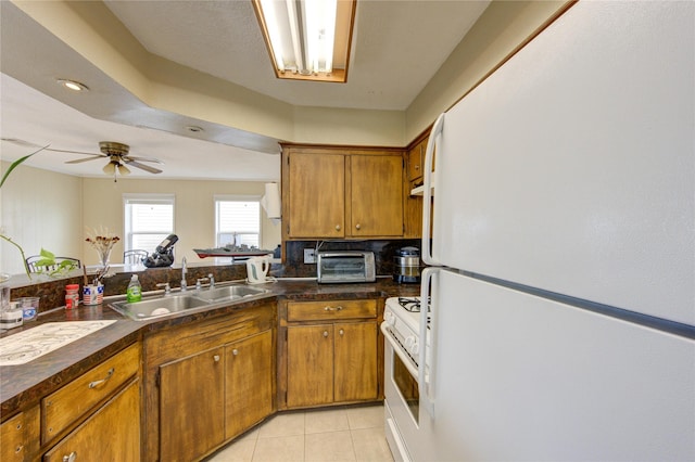 kitchen featuring dark countertops, brown cabinets, white appliances, and a sink