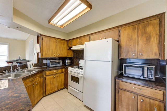 kitchen featuring under cabinet range hood, brown cabinets, white appliances, and a sink