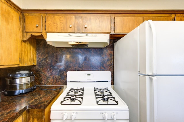 kitchen featuring under cabinet range hood, white appliances, dark countertops, and brown cabinetry