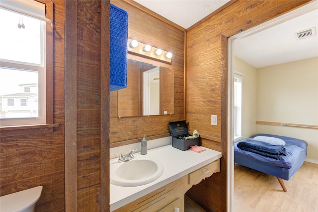 bathroom featuring visible vents, toilet, wood finished floors, wood walls, and vanity