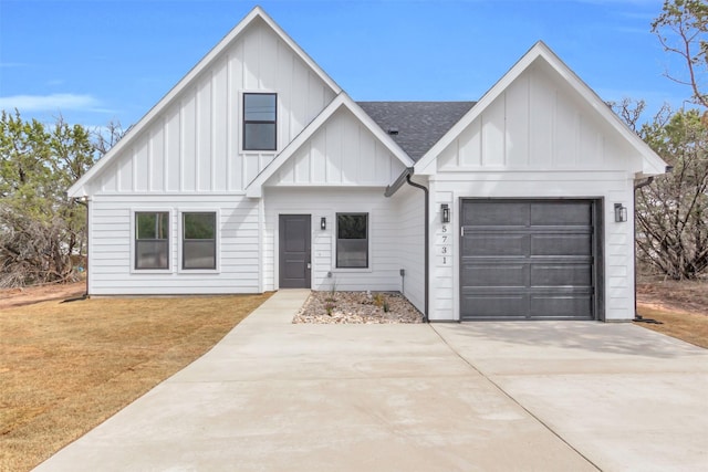 modern farmhouse featuring an attached garage, a shingled roof, a front lawn, concrete driveway, and board and batten siding