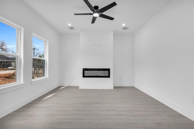 unfurnished living room with visible vents, wood finished floors, a glass covered fireplace, recessed lighting, and baseboards