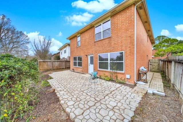 back of house with a gate, a patio area, brick siding, and a fenced backyard