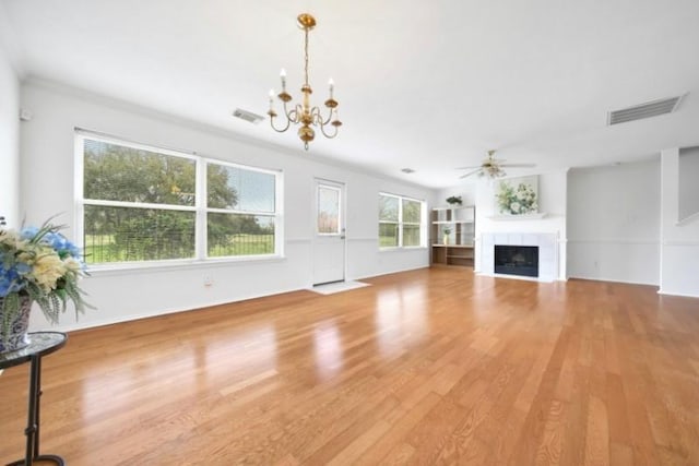 unfurnished living room with a tiled fireplace, visible vents, ceiling fan with notable chandelier, and wood finished floors