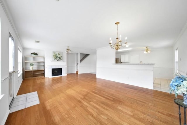 unfurnished living room with plenty of natural light, a tiled fireplace, and ceiling fan with notable chandelier