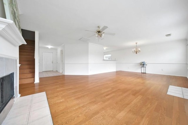 unfurnished living room featuring visible vents, wood finished floors, a fireplace, and ceiling fan with notable chandelier