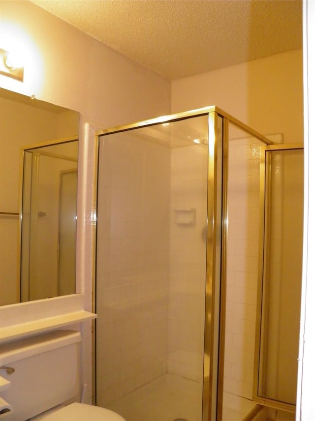 bathroom with a shower stall, toilet, and a textured ceiling