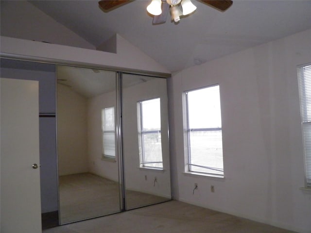 unfurnished bedroom featuring a closet, lofted ceiling, light colored carpet, and a ceiling fan