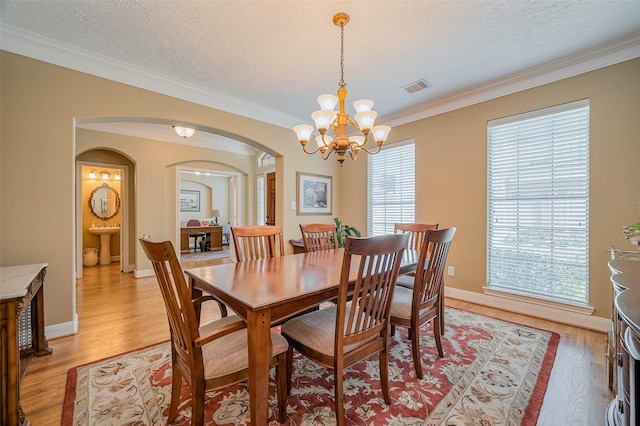 dining room featuring visible vents, crown molding, light wood-style floors, arched walkways, and a textured ceiling