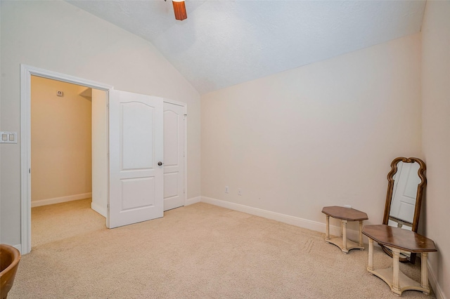 interior space with light colored carpet, a ceiling fan, baseboards, and vaulted ceiling