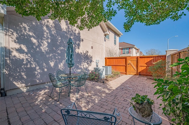 view of patio featuring cooling unit, fence, outdoor dining space, and a gate