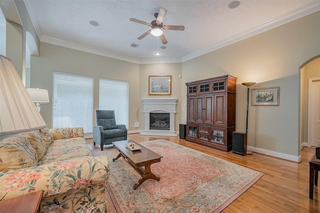 living room featuring light wood finished floors, crown molding, baseboards, arched walkways, and a glass covered fireplace