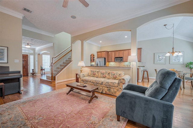 living room featuring stairway, visible vents, light wood-style flooring, crown molding, and ceiling fan with notable chandelier