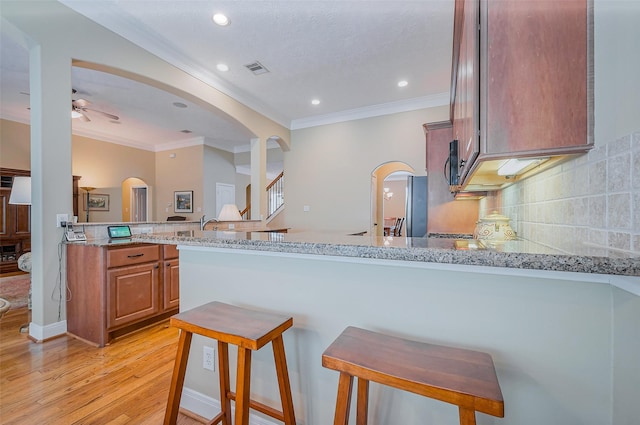 kitchen with light wood finished floors, backsplash, light stone countertops, a peninsula, and arched walkways