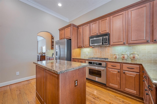 kitchen with ornamental molding, a center island, arched walkways, appliances with stainless steel finishes, and light stone countertops