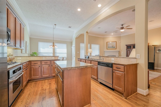 kitchen with light stone counters, a peninsula, light wood-style flooring, a sink, and stainless steel appliances