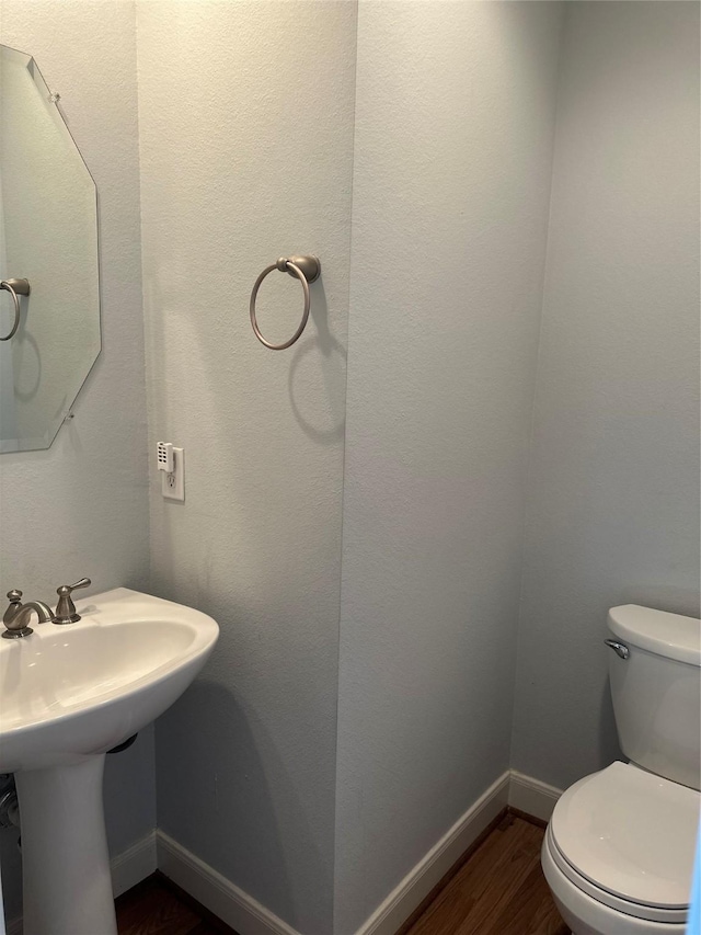 half bathroom featuring baseboards, toilet, and wood finished floors